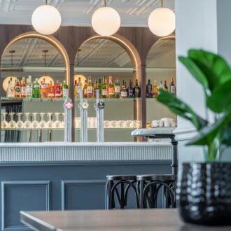 Contemporary bar area at Buile Hill Mansion featuring arched mirrored shelving with bottles and glassware, beer taps, soft globe pendant lights, and a classic panelled bar front.