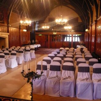 A Ceremony set up with white chair covers with a sash. A beautiful candle holder at the front of the ceremony with a view of the fire place.