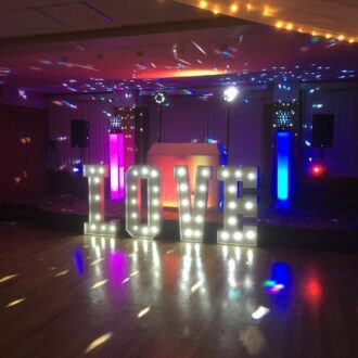 DJ set up on stage with flashing lights and large white L.O.V.E. letters in front.
