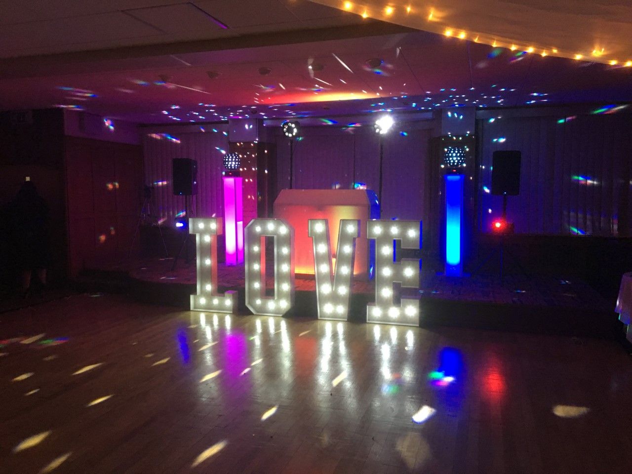 DJ set up on stage with flashing lights and large white L.O.V.E. letters in front.