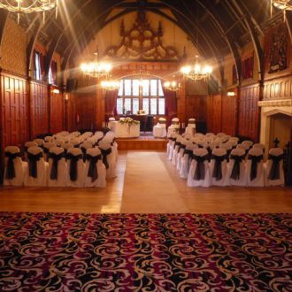 View of a ceremony at The Court House, Worsley set with white chair covers and navy sash facing the stage