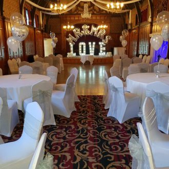 Beautifully dressed dining tables, a ceiling canopy and light up love letters on the stage along with silver Mr and Mrs balloons with a view of the dance floor.