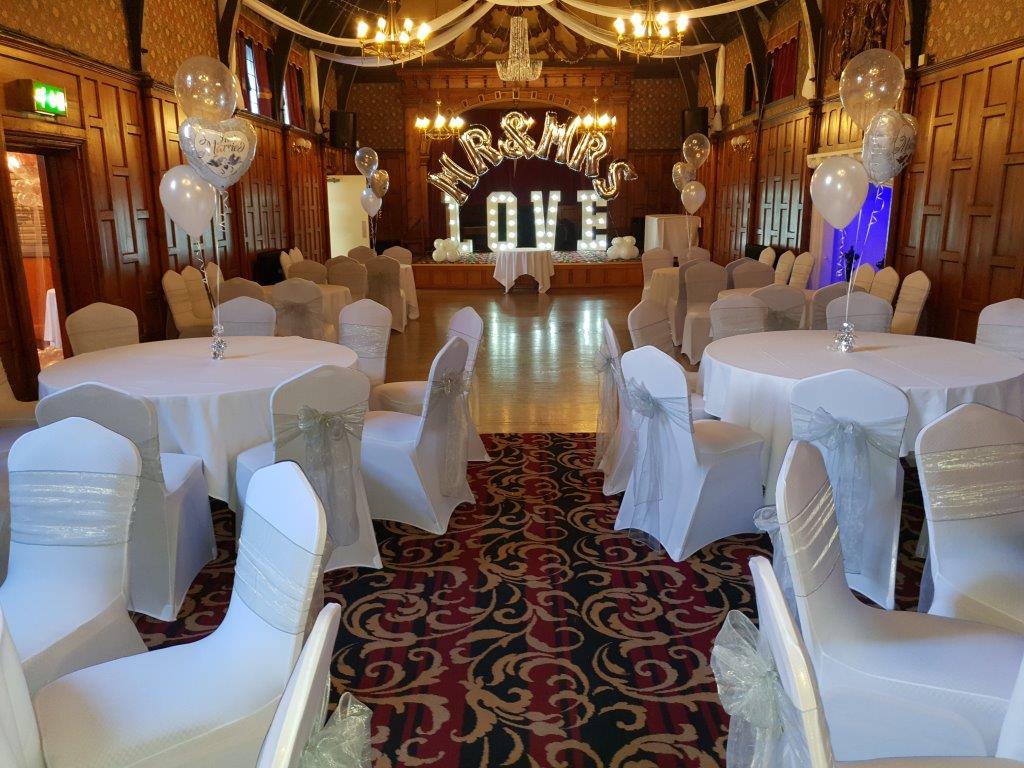 Beautifully dressed dining tables, a ceiling canopy and light up love letters on the stage along with silver Mr and Mrs balloons with a view of the dance floor.