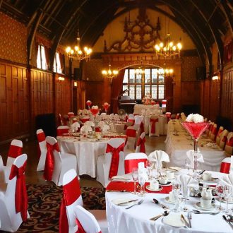 Beautifully presented dining tables with a red sash on the chairs and a red runner along the tables with large martini glass vase centerpieces.