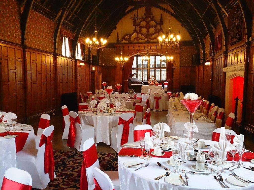Beautifully presented dining tables with a red sash on the chairs and a red runner along the tables with large martini glass vase centerpieces.