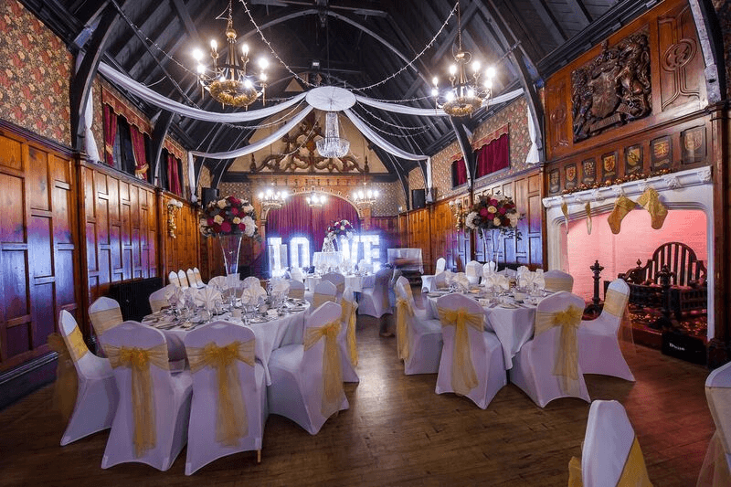 Beautifully presented dining tables for a wedding breakfast with a yellow sash on the chairs and a ceiling canopy